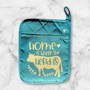 May include: Teal quilted oven mitt with a yellow silhouette of a cow and the text "Home is where the herd is" with a heart symbol.