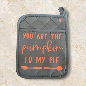 May include: A gray quilted oven mitt with the text "You are the pumpkin to my pie" in orange. The mitt has a fork and spoon graphic on the bottom.