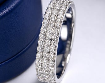 May include: A silver-toned band ring featuring three parallel rows of small, clear, round-cut stones set across the entire outer surface. The metal band has a polished, reflective finish, and the stones are arranged in a dense, uniform pattern.