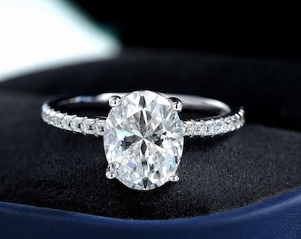 May include: A silver-toned ring featuring a large, oval-cut clear center stone held by four prongs. The slender band is encrusted with a row of small, sparkling clear stones along both sides, creating a continuous shimmering effect on the metal.