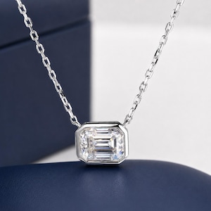 May include: A silver-toned necklace featuring a single emerald-cut clear gemstone set in a rectangular bezel setting. The pendant is suspended from a delicate, thin metal chain with small, uniform oval links that connect to the top of the setting.