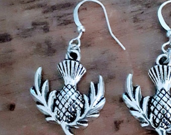 May include: A pair of silver dangle earrings featuring a detailed thistle design. The earrings have a simple hook closure.