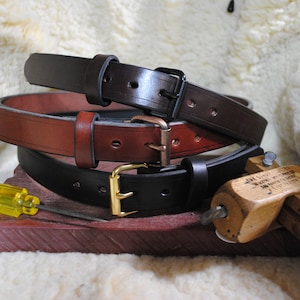 May include: Three leather belts with different colored buckles. The top belt is black with a black buckle, the middle belt is brown with a copper buckle, and the bottom belt is black with a gold buckle.