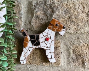 May include: A white, brown, and black mosaic tile dog sculpture with a red heart on its chest. The sculpture is mounted on a stone wall.