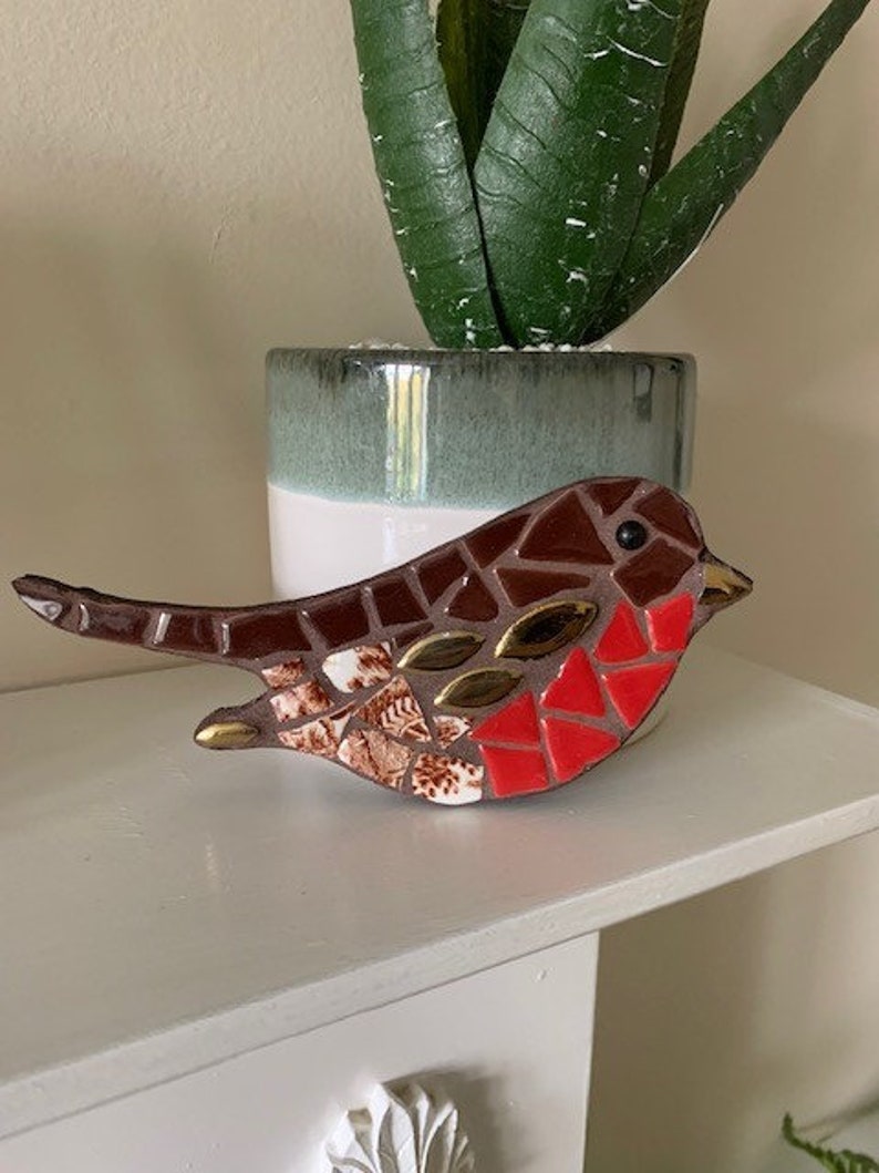 May include: A mosaic robin bird sculpture with brown, red, and gold accents. The sculpture is made of small pieces of tile and glass.