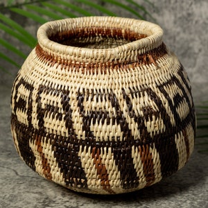 Peut inclure: Un panier tissé avec un motif géométrique brun, noir et blanc. Le panier est fait de matériaux naturels et a une forme ronde.