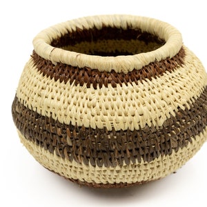 May include: A woven basket with brown and cream stripes. The basket is round and has a wide opening.