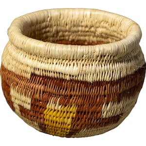 May include: A small, round woven basket with a brown, white, and yellow geometric pattern. The basket is made of natural materials and has a smooth, textured surface.