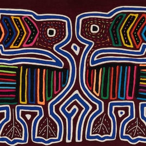 May include: A textile with a symmetrical design of two bird-like figures. The figures are outlined in blue and white, with colourful geometric patterns in orange, yellow, green, and pink. The background is a deep burgundy colour.