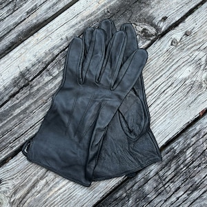 May include: A pair of black leather gloves, folded and laid out on a weathered wooden surface.