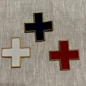 May include: Three embroidered patches in the shape of a plus sign. The patches are red, white, and black with gold trim.