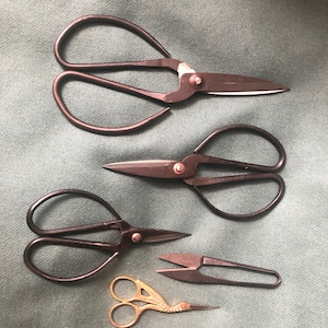 May include: Four pairs of scissors on a green fabric background. The scissors are all different sizes and styles. One pair is gold, and the other three are black.