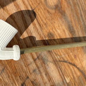 May include: A white, curved tobacco pipe with a ribbed bowl and a wooden stem. The pipe is resting on a wooden surface, with a shadow cast to the side. The pipe is a classic smoking accessory.