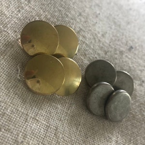 May include: A group of four round, gold-colored buttons and a group of four round, silver-colored buttons. The buttons are arranged in two groups, one on top of the other.
