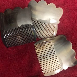 May include: Three horn combs with a wavy top and fine teeth are displayed on a red surface. The combs vary in colour, with one being dark brown, and the others are light brown and translucent.