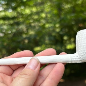 Puede incluir: Una pipa de tabaco blanca que presenta un hornillo texturizado con un patrón de rejilla y una boquilla con una textura lineal similar a la veta de la madera. La pipa es de color blanco sólido y tiene un acabado mate suave en toda su superficie.