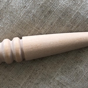 May include: A wooden tool with a rounded handle and a tapered point. The handle has a series of ridges for a better grip.