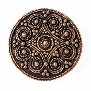 May include: A round, gold-colored metal button with a detailed design of interlacing spirals and dots.