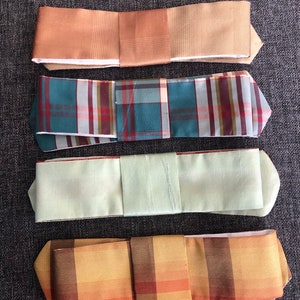 Puede incluir: Cuatro pajaritas de diferentes patrones y colores. Las pajaritas están dobladas y dispuestas sobre una superficie gris texturizada. Las pajaritas están hechas de seda y tienen una variedad de colores, incluyendo marrón, verde, beige y naranja.
