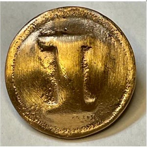 Op de afbeelding: Een ronde knoop in antieke stijl met een getextureerde, goud-bronzen afwerking. De knoop toont de letter "T" in een gestileerd, licht verhoogd ontwerp. De randen hebben een gedetailleerde, geribbelde rand.
