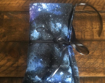 May include: A black fabric pouch with a blue and white galaxy print. The pouch is tied with a black ribbon.