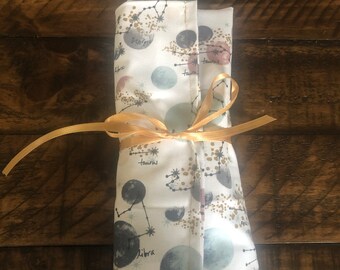 May include: A white fabric pouch with a gold ribbon tied around it. The pouch is decorated with a constellation pattern and the words "Libra", "Taurus", and "Scorpio".