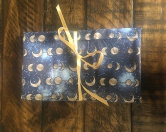 May include: A blue fabric pouch with a gold ribbon tied around it. The pouch has a pattern of gold moons and stars on a dark blue background.