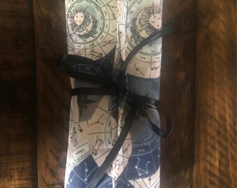 May include: A rolled up fabric pouch with a celestial design featuring constellations and planets. The pouch is tied with a black ribbon.