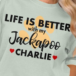 May include: A light green t-shirt with the text "LIFE IS BETTER with my Jackapoo CHARLIE" in black script and a paw print design. The word "CHARLIE" has a red heart on each side.