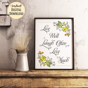 May include: A black framed print with a white background and a floral design in yellow, green, and orange. The print features the text "Live Well Laugh Often Love Much".