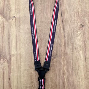 May include: A navy blue lanyard with the text "BMW Motorsport" in white. The lanyard has red and white stripes down the center and a black clasp with a key ring. The lanyard is displayed on a wooden surface.