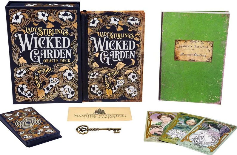 May include: An oracle deck set with a dark blue box and book featuring gold floral designs and the title "Lady Stirling's Wicked Garden." Includes a green journal, cards, a key, and a card with the Muriel Stirling Foundation logo.