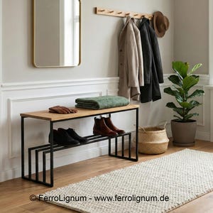 Könnte beinhalten: Moderner Eingangsbereich mit einer Holzbank und einem schwarzen Metallrahmen. Auf der Bank liegen Schuhe, Handschuhe und ein grünes Handtuch. Mäntel und ein Hut hängen an einer Wandgarderobe. Eine Topfpflanze und ein Weidenkorb ergänzen die Einrichtung.