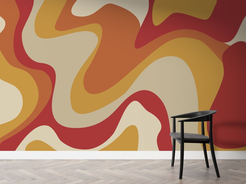 Op de afbeelding: Een zwarte stoel staat voor een muur met een abstract patroon in retro-stijl. Het patroon heeft draaiende vormen in tinten rood, oranje en geel.