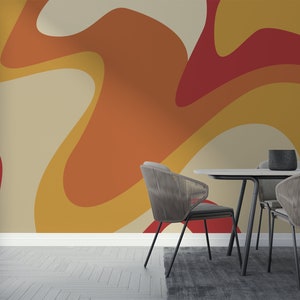 Op de afbeelding: Een eetkamer met een moderne abstracte behang met een draaiende patroon in tinten van oranje, geel en rood. Het behang is achter een witte tafel met vier zwarte stoelen.