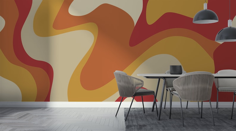 Op de afbeelding: Een eetkamer met een moderne abstracte behang met een draaiende patroon in tinten van oranje, geel en rood. Het behang is achter een witte tafel met vier zwarte stoelen.