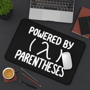 May include: Black rectangular mouse mat with the text "POWERED BY (λ) PARENTHESES" in white. A white mouse sits on the mat. A laptop, notebooks, pencils, and a coffee cup are also on the dark surface.