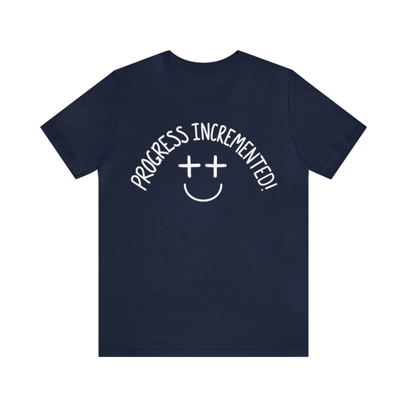 May include: Navy blue t-shirt with white text that reads "Progress incremented!" and a smiley face with two plus signs for eyes.