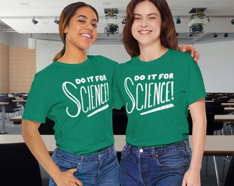Op de afbeelding: Twee mensen dragen bijpassende groene t-shirts met de tekst "DO IT FOR SCIENCE!" in het wit. De shirts worden gecombineerd met een blauwe jeans. De achtergrond lijkt een klaslokaal of collegezaal te zijn.