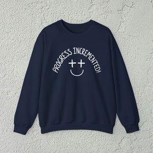 May include: A navy blue sweatshirt with white text that reads "Progress incremented!" with a smiley face with two plus signs for eyes.