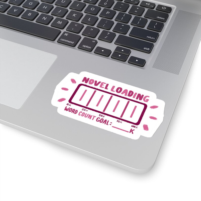 Peut inclure: Un autocollant rose et blanc avec une barre de progression qui indique "NOVEL LOADING" et "WORD COUNT GOAL: ___ K". La barre de progression est remplie de rose et indique 75% de compl&eacute;tude.