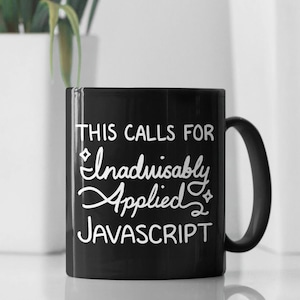 May include: Black ceramic mug with white text: "THIS CALLS FOR Inadvisably Applied JAVASCRIPT." The mug has a black handle. The background is blurred, featuring a white pot with a plant and white vertical panels.