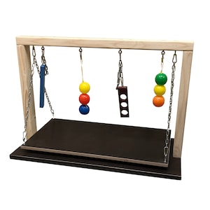 Könnte beinhalten: Holzrahmen für sensorisches Spiel mit einer braunen Plattform und hängenden Spielzeugen. Die Spielzeuge umfassen einen blauen und gelben Ball, einen roten und gelben Ball, einen grünen und gelben Ball und eine rote rechteckige Form mit Löchern.