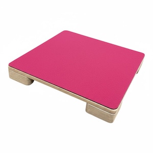 May include: A rectangular, cerise laptop stand with a textured surface. The stand is supported by four light-coloured wooden feet. The edges of the stand are a dark colour.