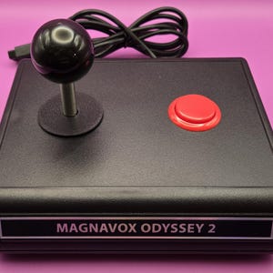 May include: A black joystick with a red button and a black knob. The joystick is labeled "MAGNAVOX ODYSSEY 2".