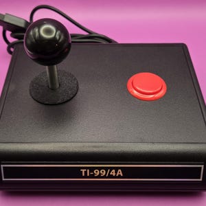 May include: A black joystick with a red button and a black knob. The joystick is labeled "TI-99/4A".