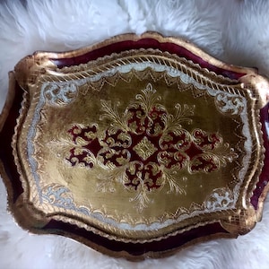 May include: An ornate rectangular serving tray featuring a deep burgundy border and a central gold panel. The surface is decorated with intricate gold filigree patterns, embossed textures, and scalloped edges with integrated side handles.