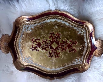 May include: An ornate rectangular serving tray featuring a deep burgundy border and a central gold panel. The surface is decorated with intricate gold filigree patterns, embossed textures, and scalloped edges with integrated side handles.