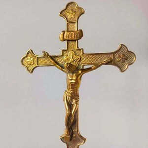 May include: A gold-toned metal crucifix featuring a central figure of Jesus on the cross. The cross has textured arms with star motifs at the ends and a banner at the top displaying the letters INRI. The design includes a star behind the head.