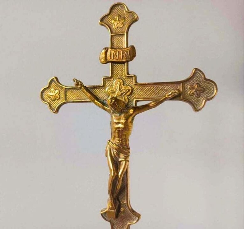 May include: A gold-toned metal crucifix featuring a central figure of Jesus on the cross. The cross has textured arms with star motifs at the ends and a banner at the top displaying the letters INRI. The design includes a star behind the head.